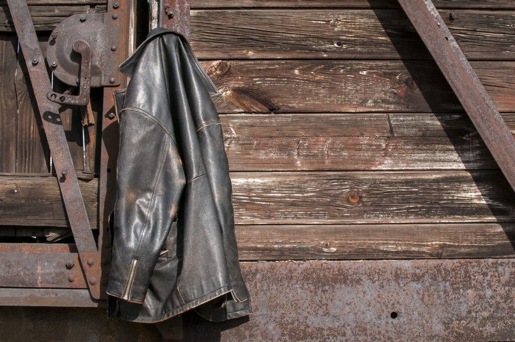 Vintage leather male jacket hanging on wooden railway wagon wall
